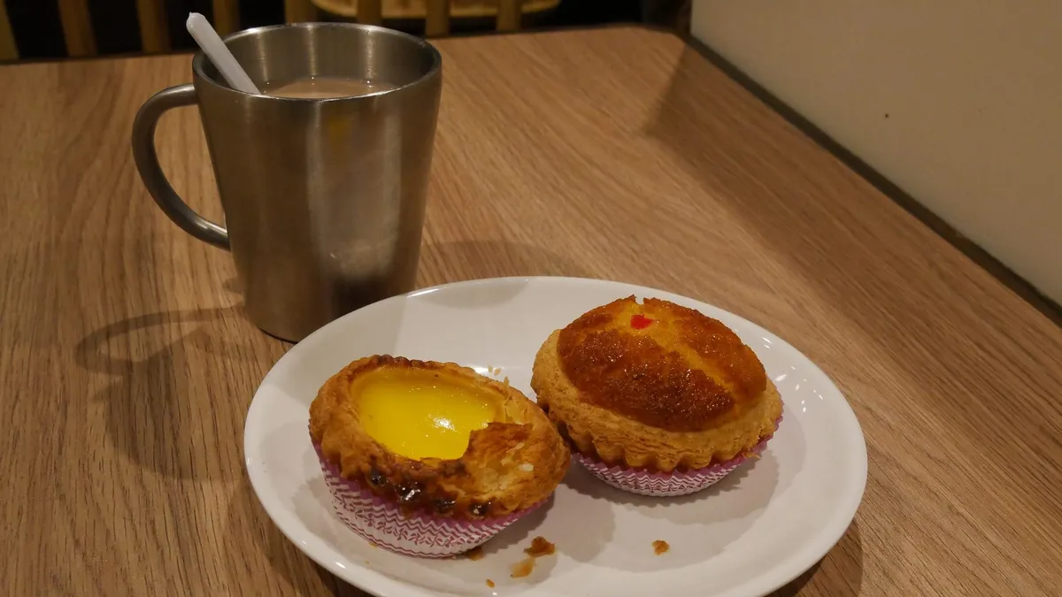 An egg tart and a cup of milk tea on a café table
