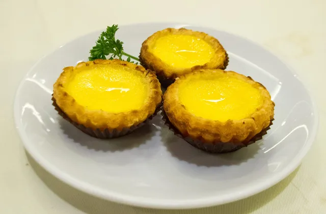 Three golden egg tarts on a white plate