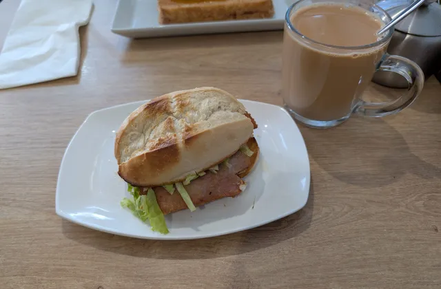 A pork chop bun and a cup of milk tea on a wooden table